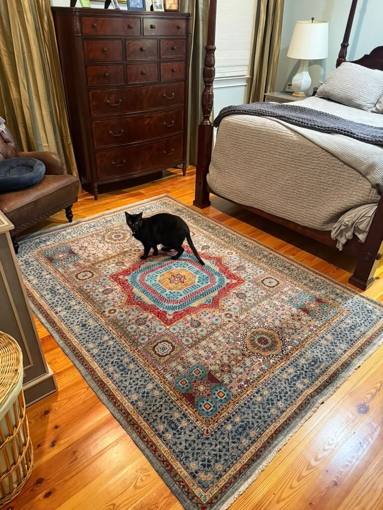 A Mamluk-pattern bedroom rug with a soft grey and red palette on pine flooring.
