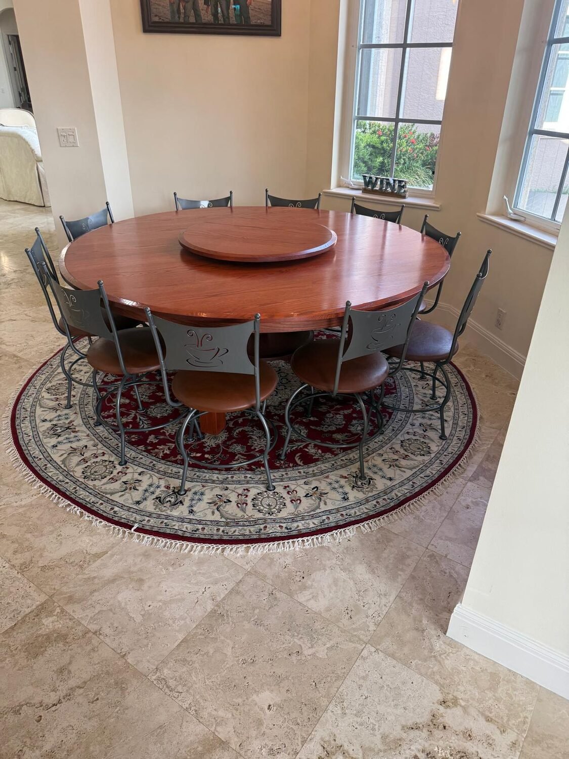 A round red floral rug sized to a large round dining table with ten chairs.