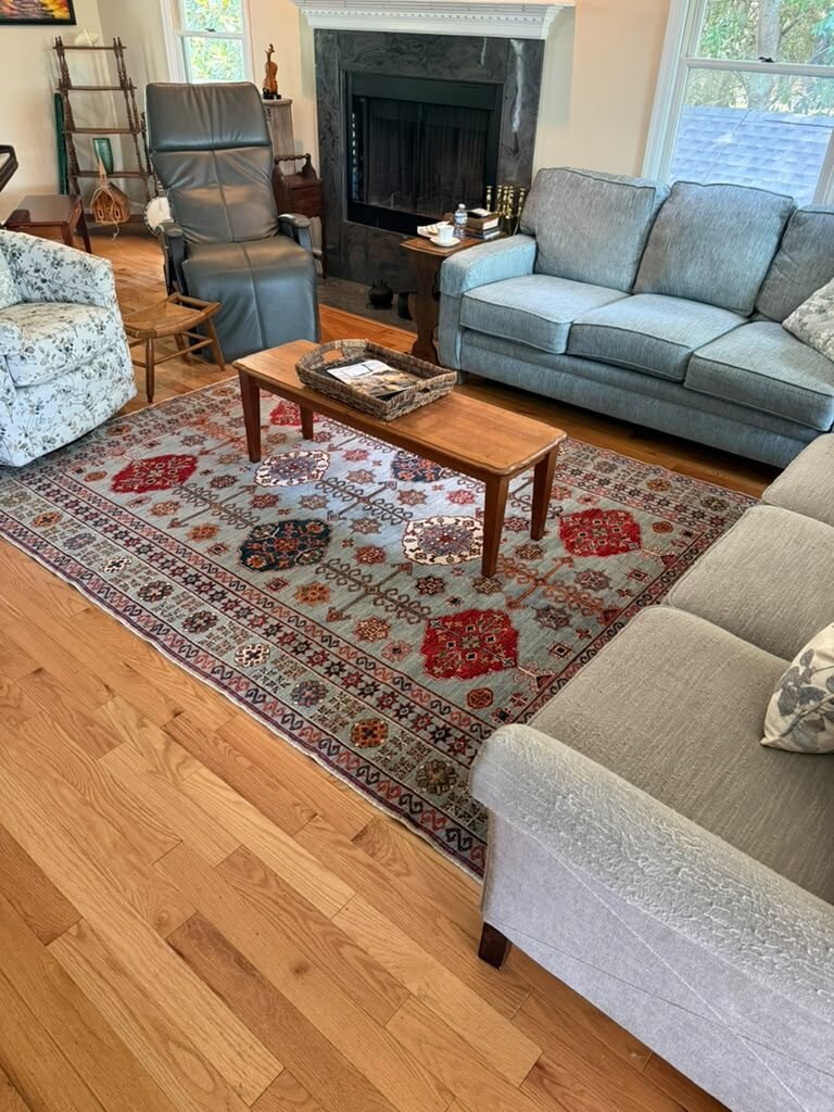 A soft blue tribal rug with red medallions in a living room with oak floors and a low wooden bench.