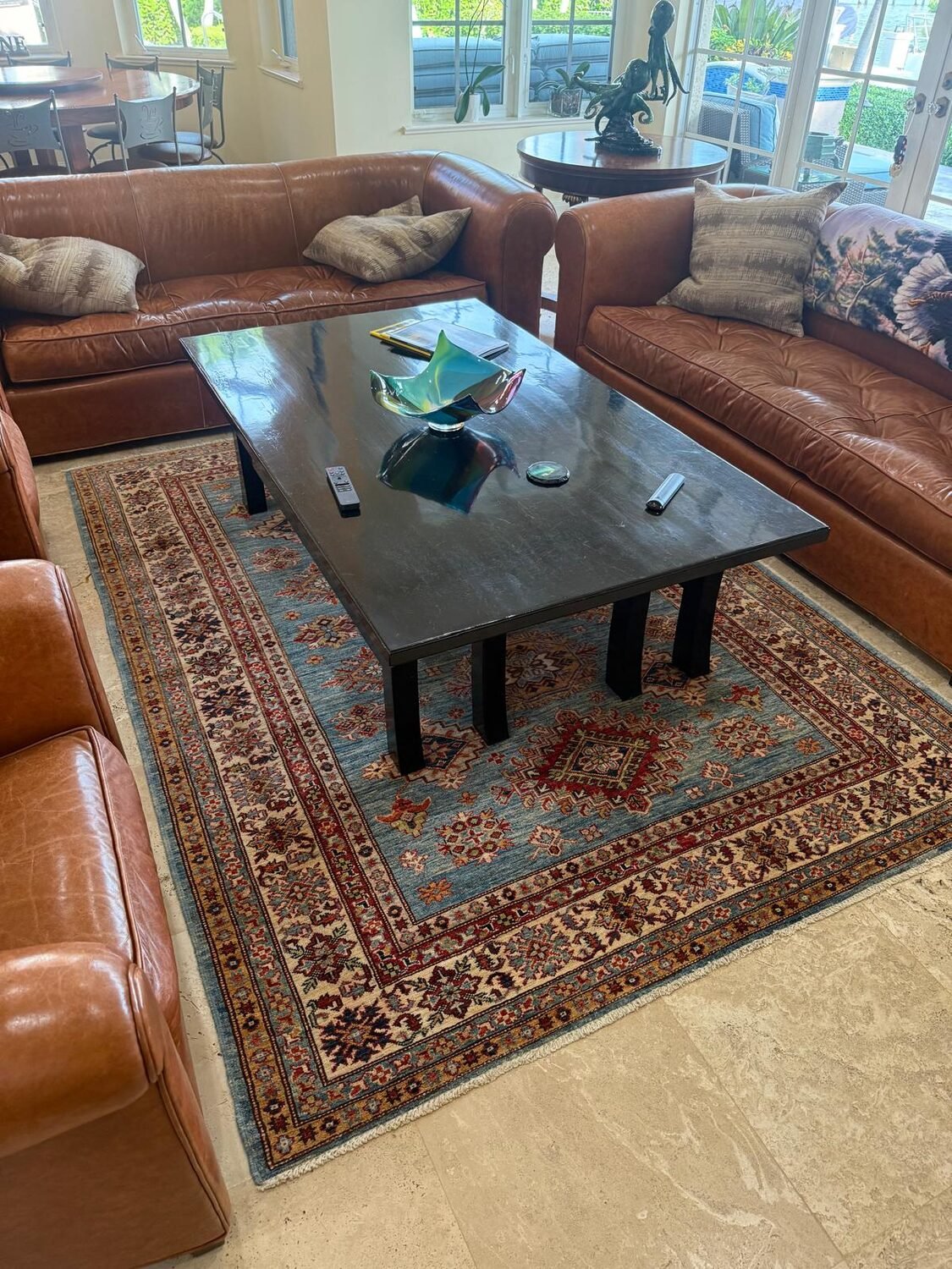 A blue Kazak rug between leather sofas, sized to hold the full seating arrangement.