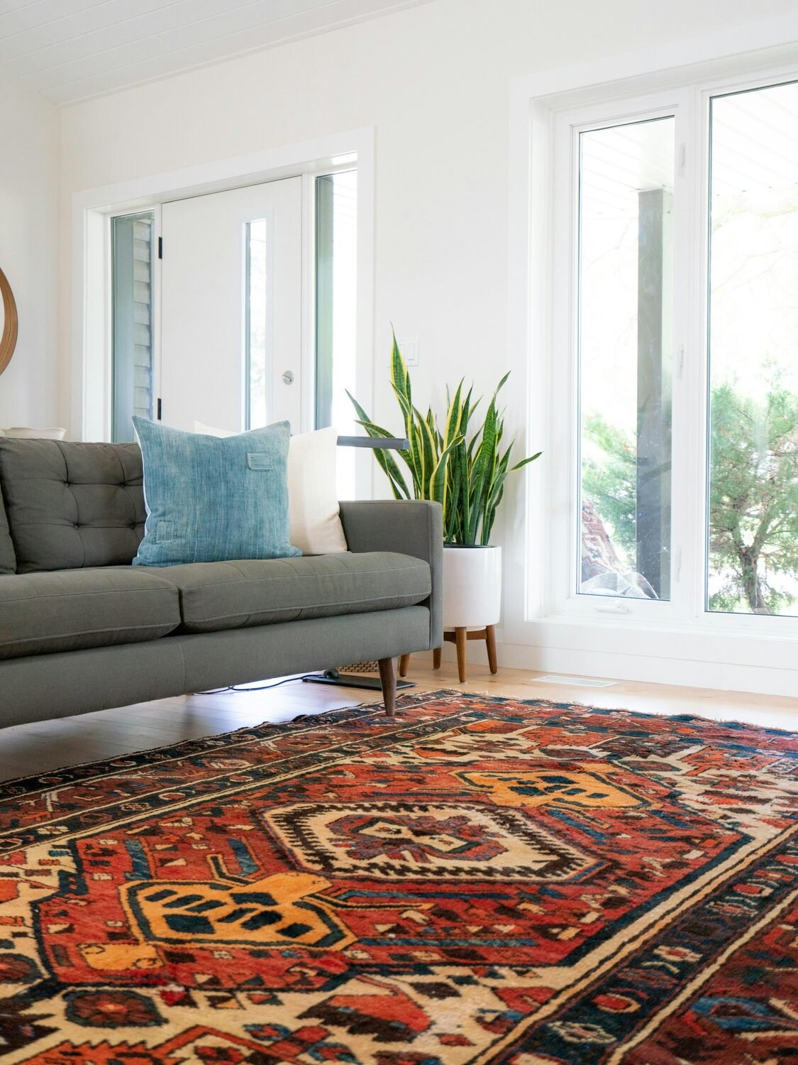 A warm red and rust Heriz-style rug anchoring a bright living room with a low sofa and tall windows.