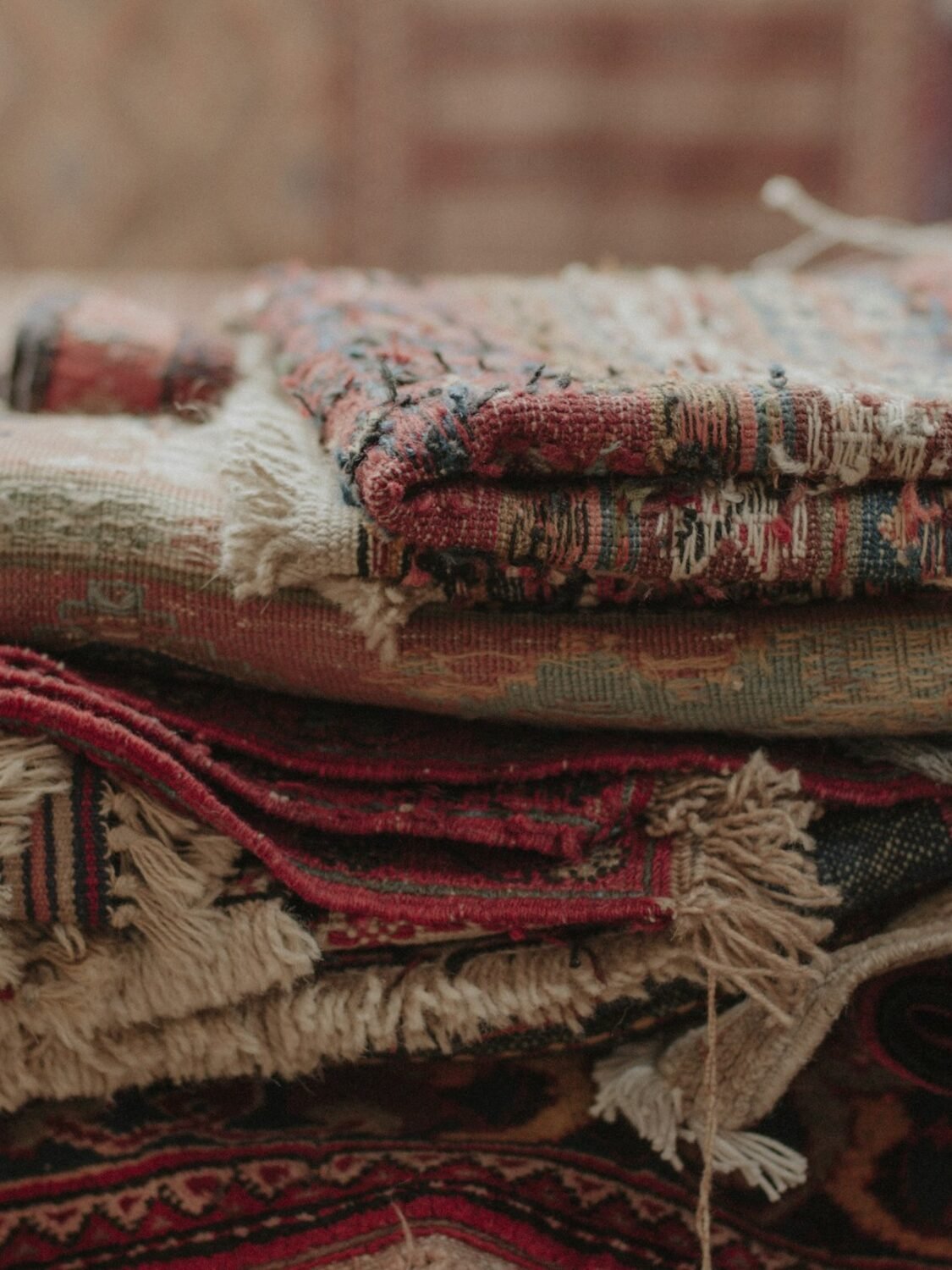 A stack of folded hand-knotted rugs with visible fringes, layered by pattern and colour.